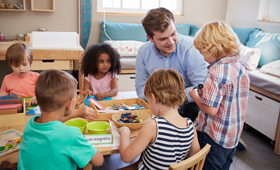 Erzieher mit Kindern an einem Tisch in einer Kindertageseinrichtung