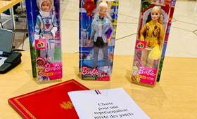 Fassung der „Charta für eine ausgewogene Geschlechterdarstellung bei Spielwaren“, dahinter drei verschiedene Barbie-Figuren