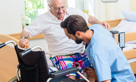Junger Pfleger hilft Senior vom Bett in den Rollstuhl