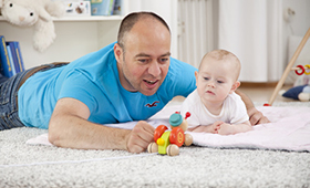 Vater spielt mit Baby im Kinderzimmer auf einem Teppich