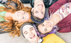 Vier Jugendliche, zwei Jungs und zwei Mädchen, sternförmig auf dem Boden liegend, von oben fotografiert