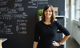 Eine Frau steht in einem modernen Büro vor einer schwarzen mit weißem Text beschrifteten Tafel im Hintergrund