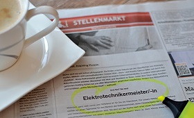 Mit einem gelben Textmarker markierte Stellenanzeige in einer Zeitung, links daneben eine Tasse Kaffe, rechts der Marker