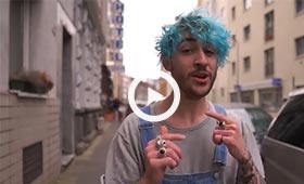Vorschaubild des Videos mit youtuber Toni Pirosa, der mit Latzhose und blau gefärbten Haaren eine Straße entlang geht und in die Kamera singt