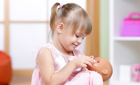 Mädchen in rosa gekleidet mit einer Babypuppe im Arm